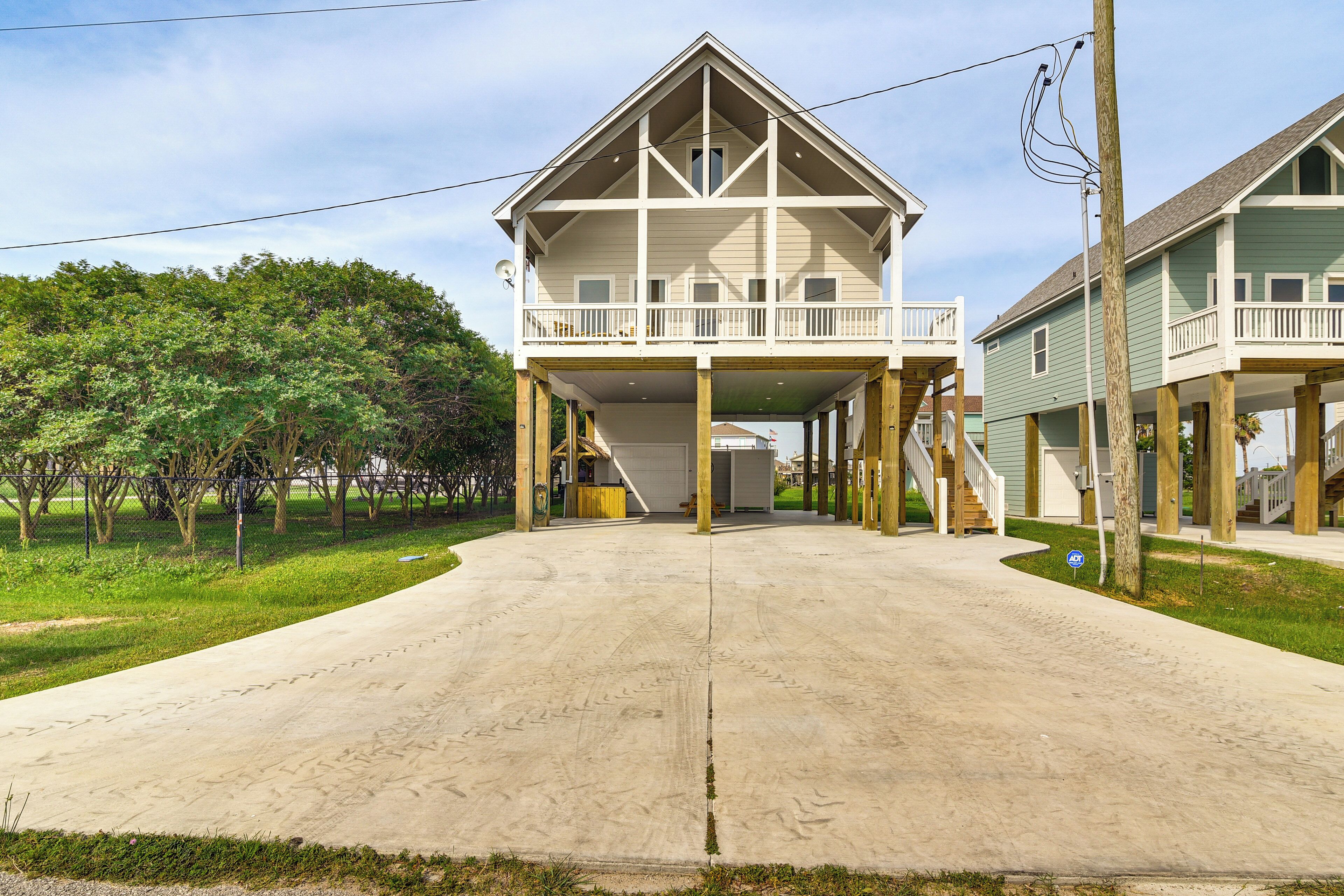 A two-story house with a balcony, a driveway, and a grassy area with trees.
