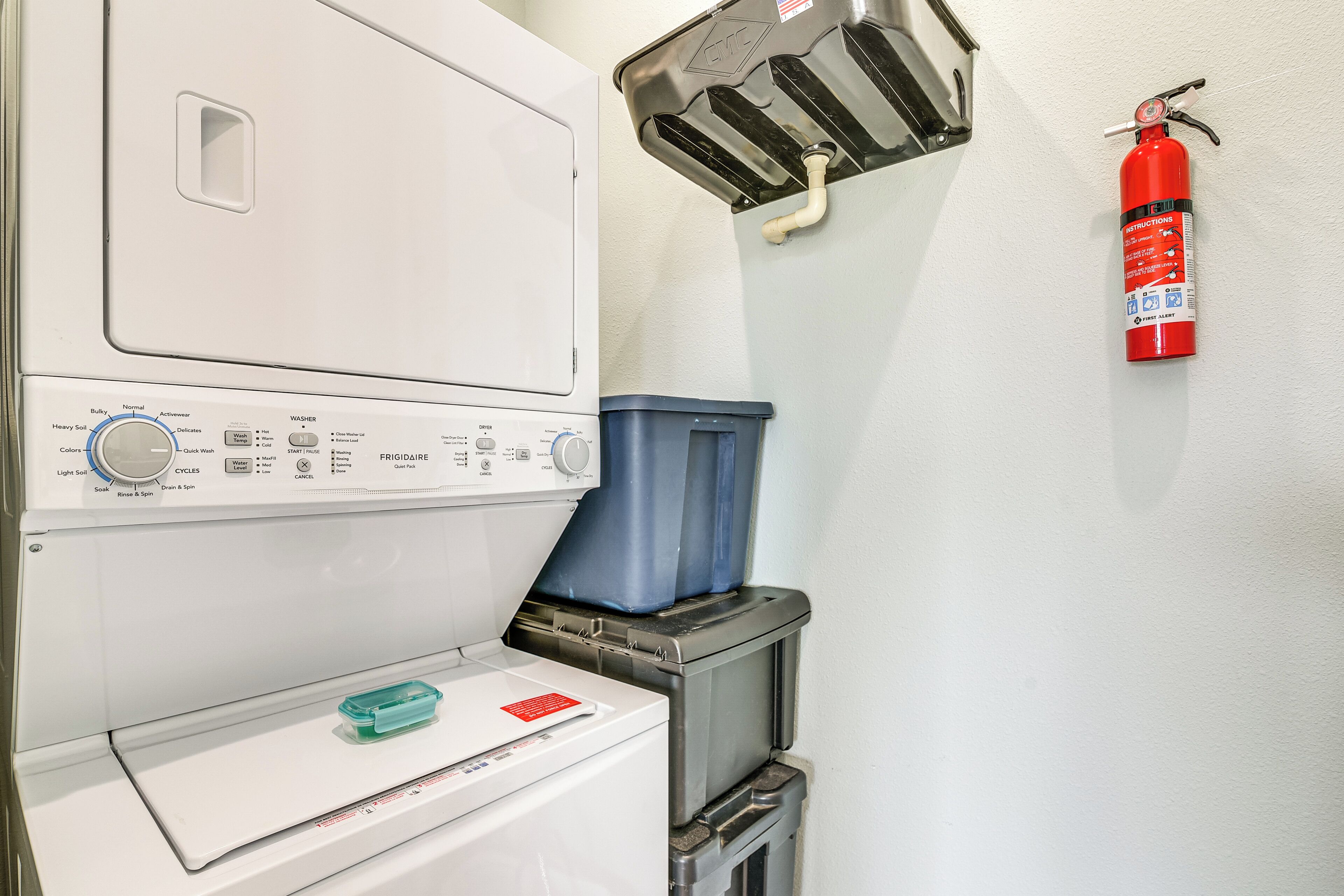 A laundry area with a front-loading washer, a dryer, and a fire extinguisher mounted on the wall.