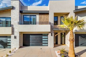 Une maison moderne à deux étages, dotée d’un garage, d’un balcon et d’un palmier dans le jardin.