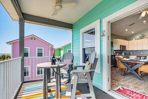 A balcony with a table and chairs, a view of colorful houses, and a kitchen area visible through an open door.