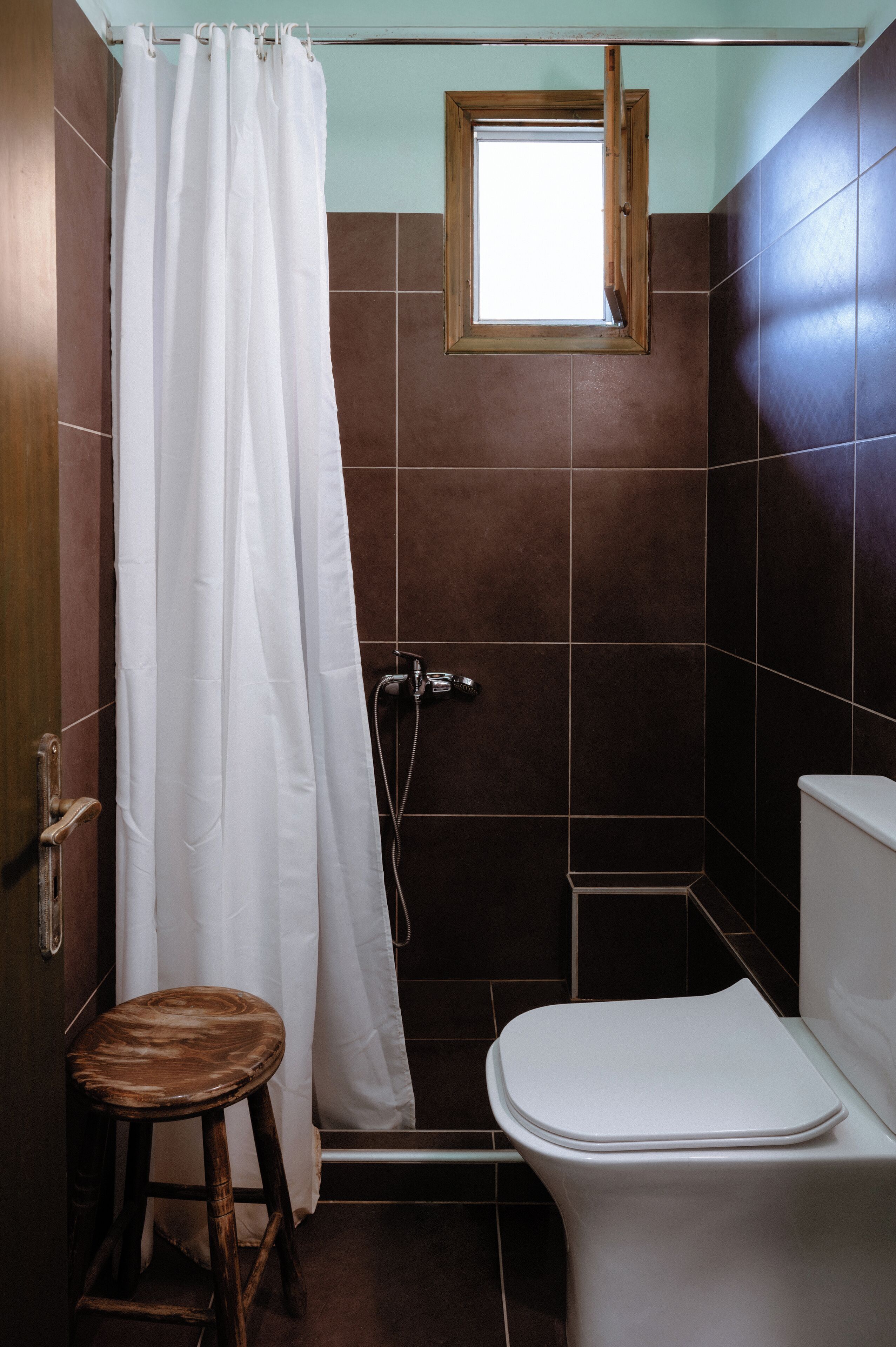 Une salle de bain avec une douche, des toilettes et un petit tabouret.