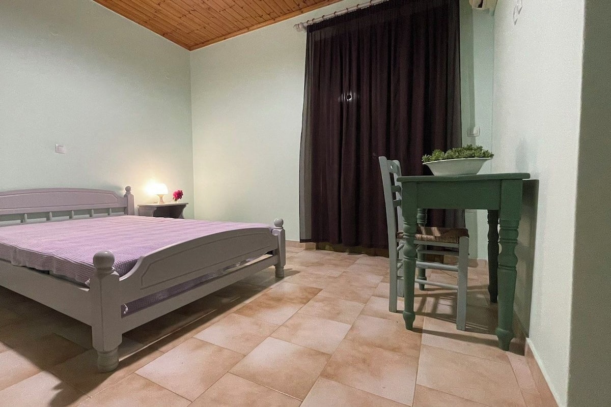 Un dormitorio con cama, mesita de noche, lámpara, silla y una mesa con planta.