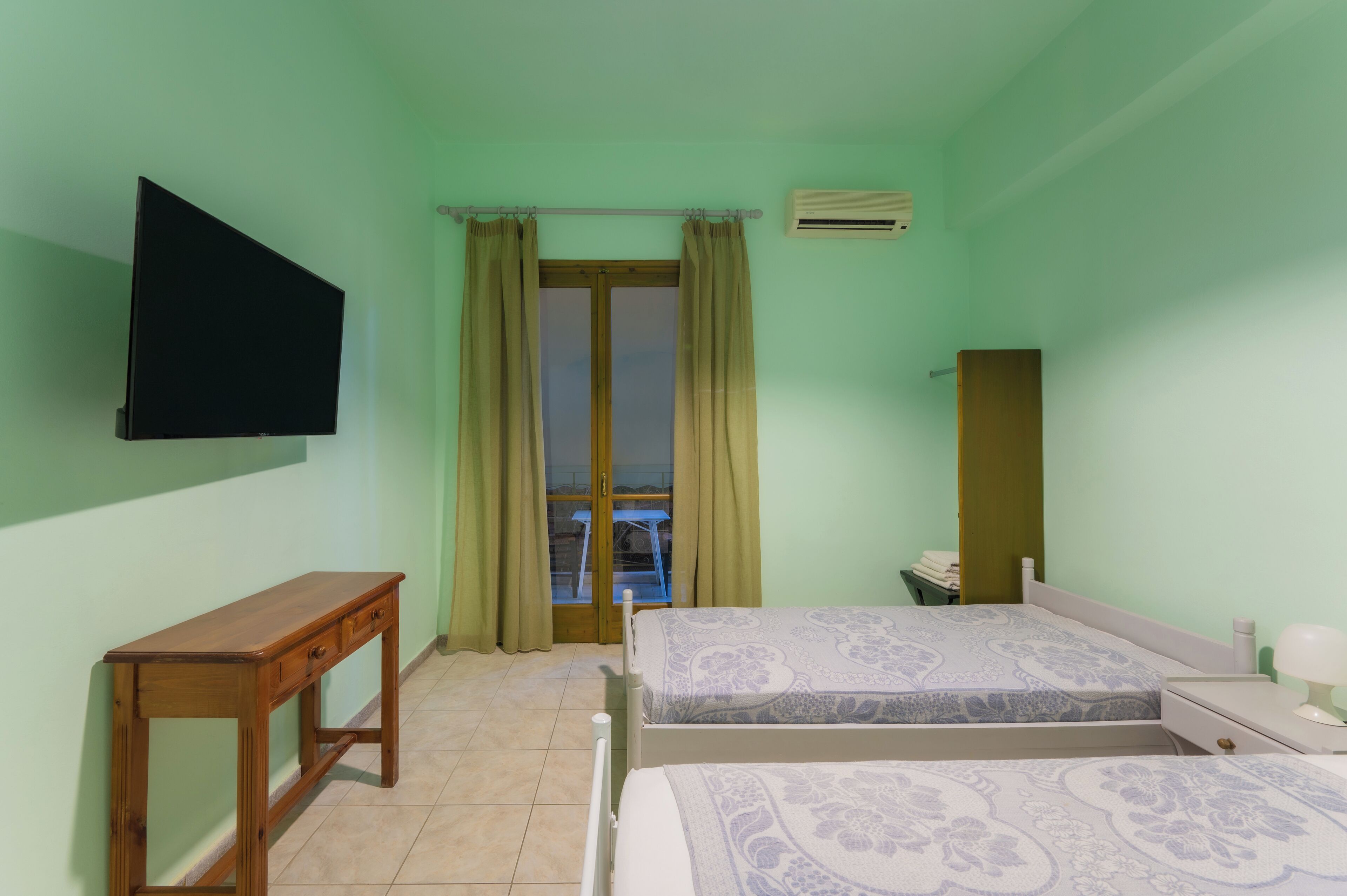 Un dormitorio con cama, mesita de noche y televisor instalado en la pared.