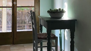 A room with a wooden ceiling, a window with a view of a tree, a table with a potted plant, a chair, and an air conditioning unit mounted on the wall. - Old Boat (Nikiana)