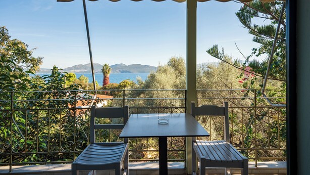A balcony with a table and two chairs, overlooking a scenic view of the sea and mountains. - Old Boat (Nikiana)