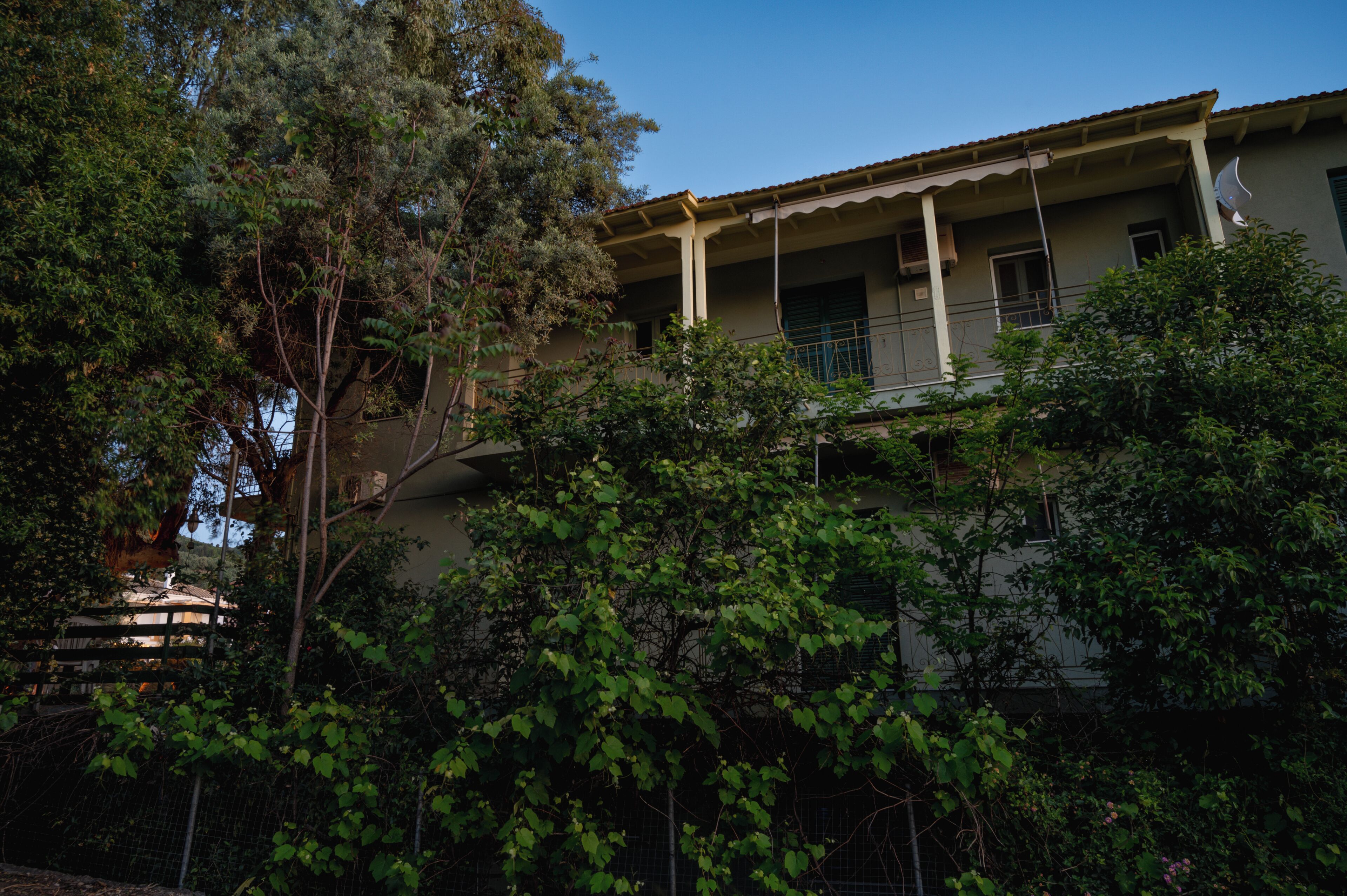 A two-story building with a balcony, surrounded by dense foliage.