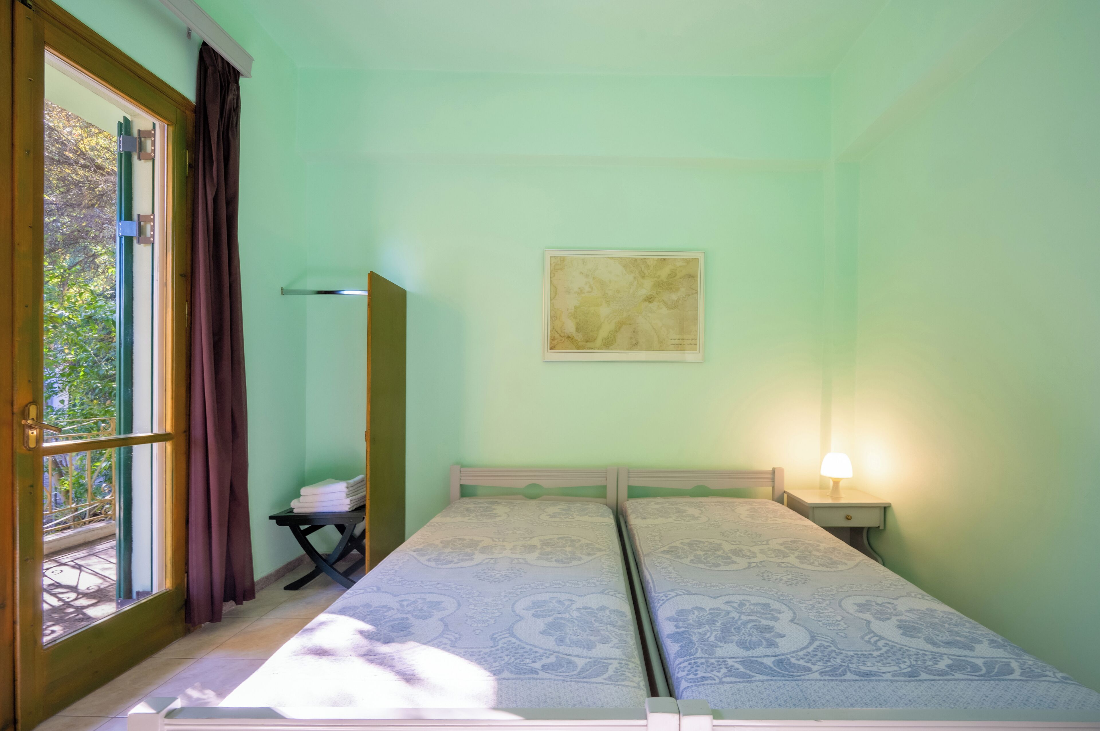 A room with two beds, a window with curtains, a map on the wall, and a nightstand with a lamp.