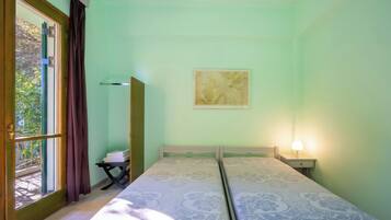 A room with two beds, a window with curtains, a map on the wall, and a nightstand with a lamp.