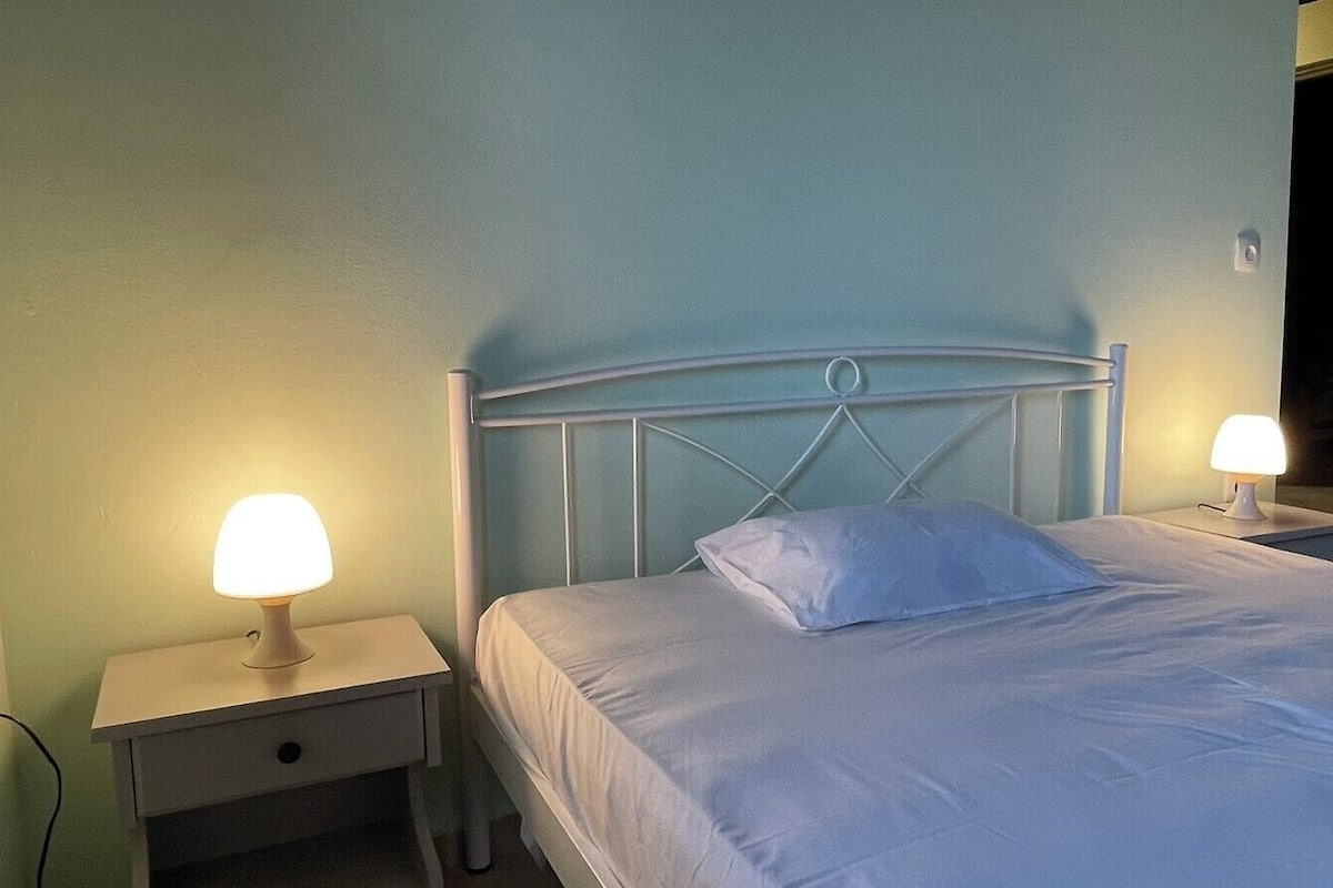 Una cama bien tendida con sábanas blancas y una sola almohada, flanqueada por dos mesitas de noche con lámparas.