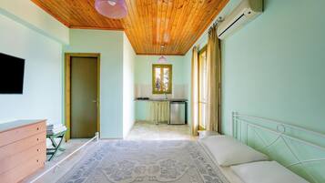 Un dormitorio con techo de madera, cama, cómoda, pequeña cocina americana y ventana.