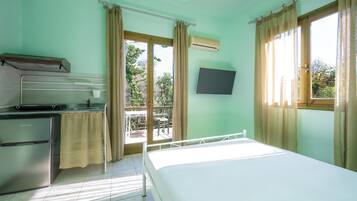A room with a bed, a small kitchenette, a TV, and a balcony with curtains.