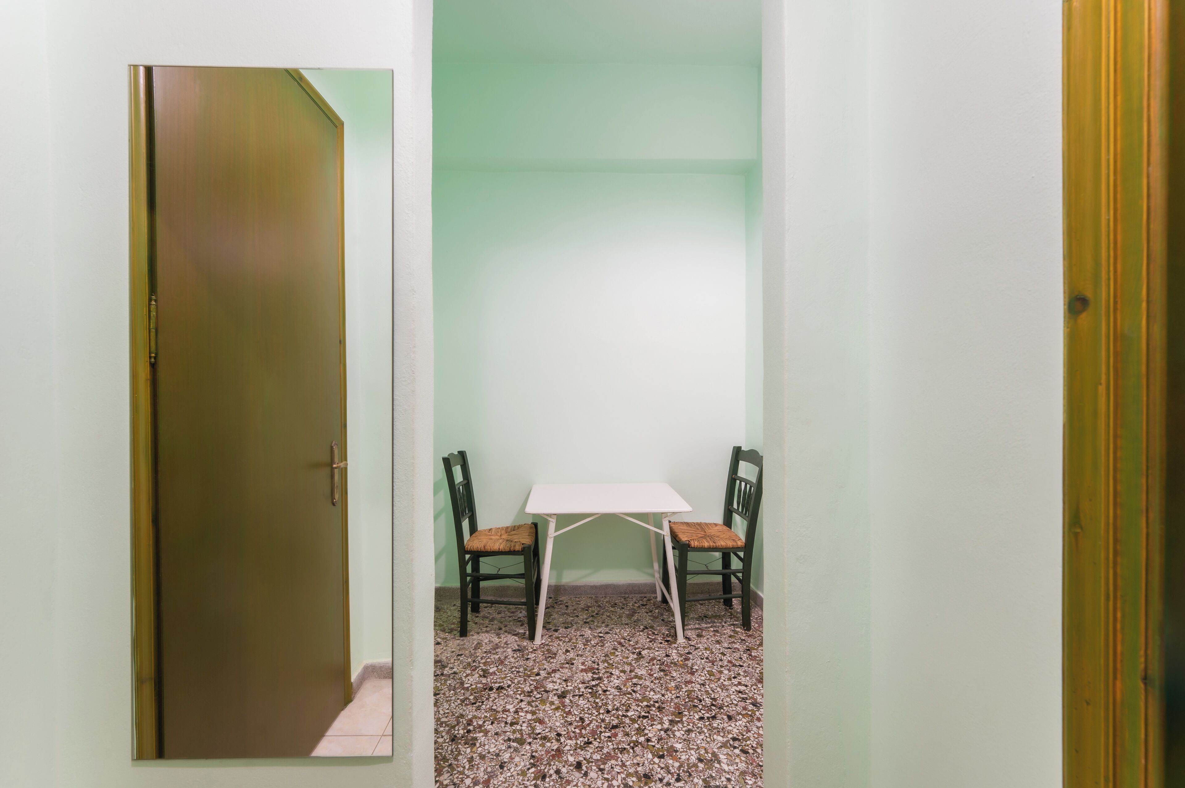 Una habitación con una mesa blanca y dos sillas, una puerta y una pared verde.