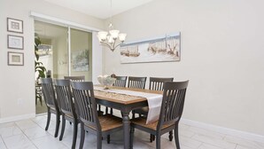 A dining room with a wooden table, six chairs, a chandelier, and a painting on the wall. - Wonderful 4Bd With Pool at Storey Lake Resort 4819 (Kissimmee)