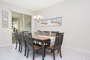 A dining room with a wooden table, six chairs, a chandelier, and a painting on the wall.