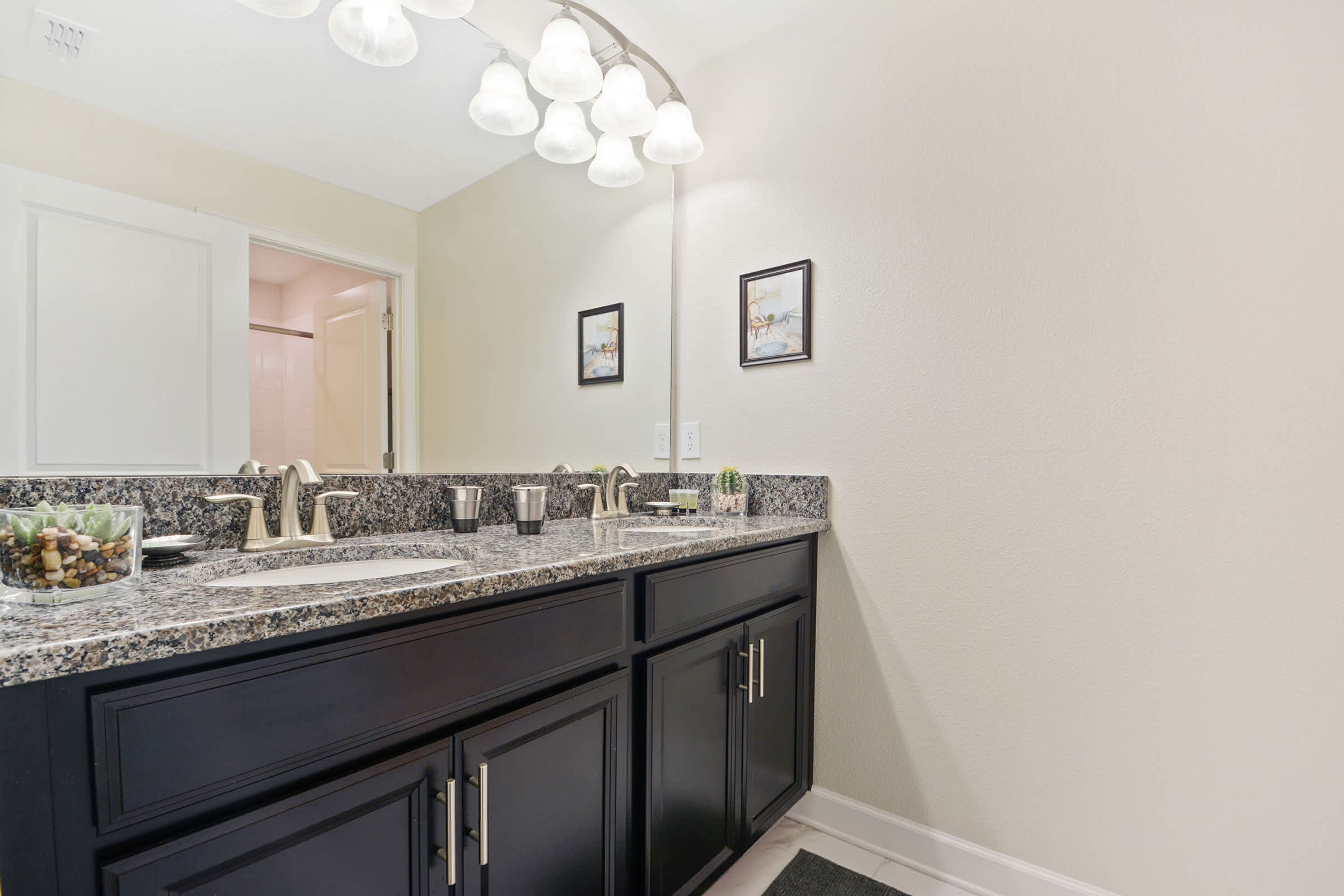A modern bathroom with a granite countertop, dark cabinetry, and a large mirror.