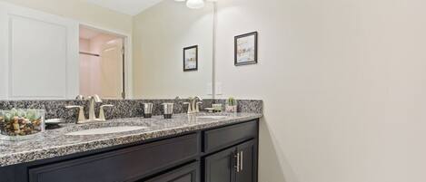 A modern bathroom with a granite countertop, dark cabinetry, and a large mirror.