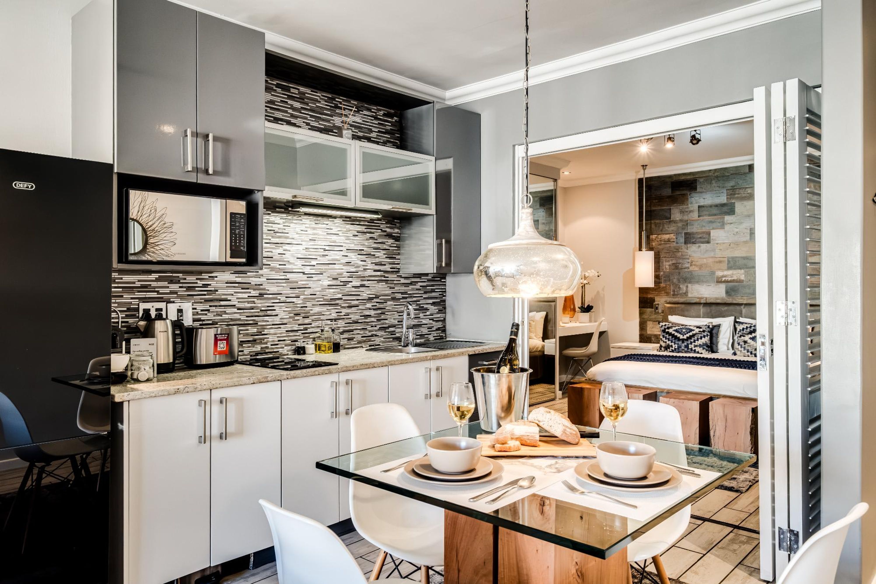 A modern kitchen with a glass dining table, white chairs, and a built-in microwave.