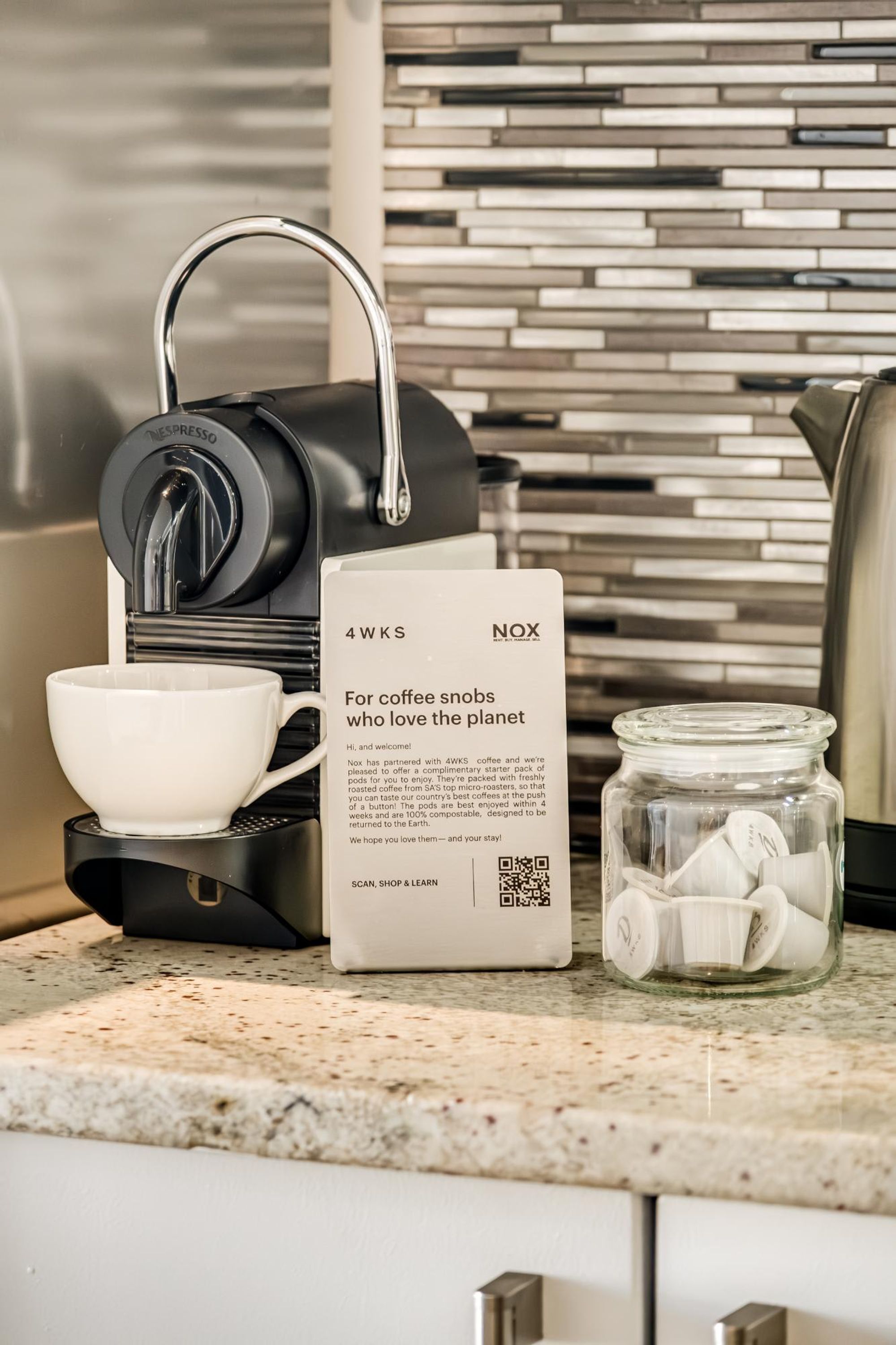 A coffee machine, a 4WKS coffee pod pack, and a jar of coffee pods on a kitchen counter.