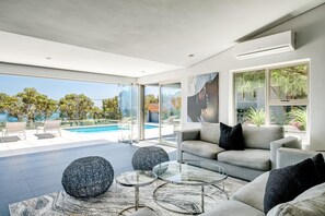 A modern living room with a pool view, grey sofas, and a glass coffee table.