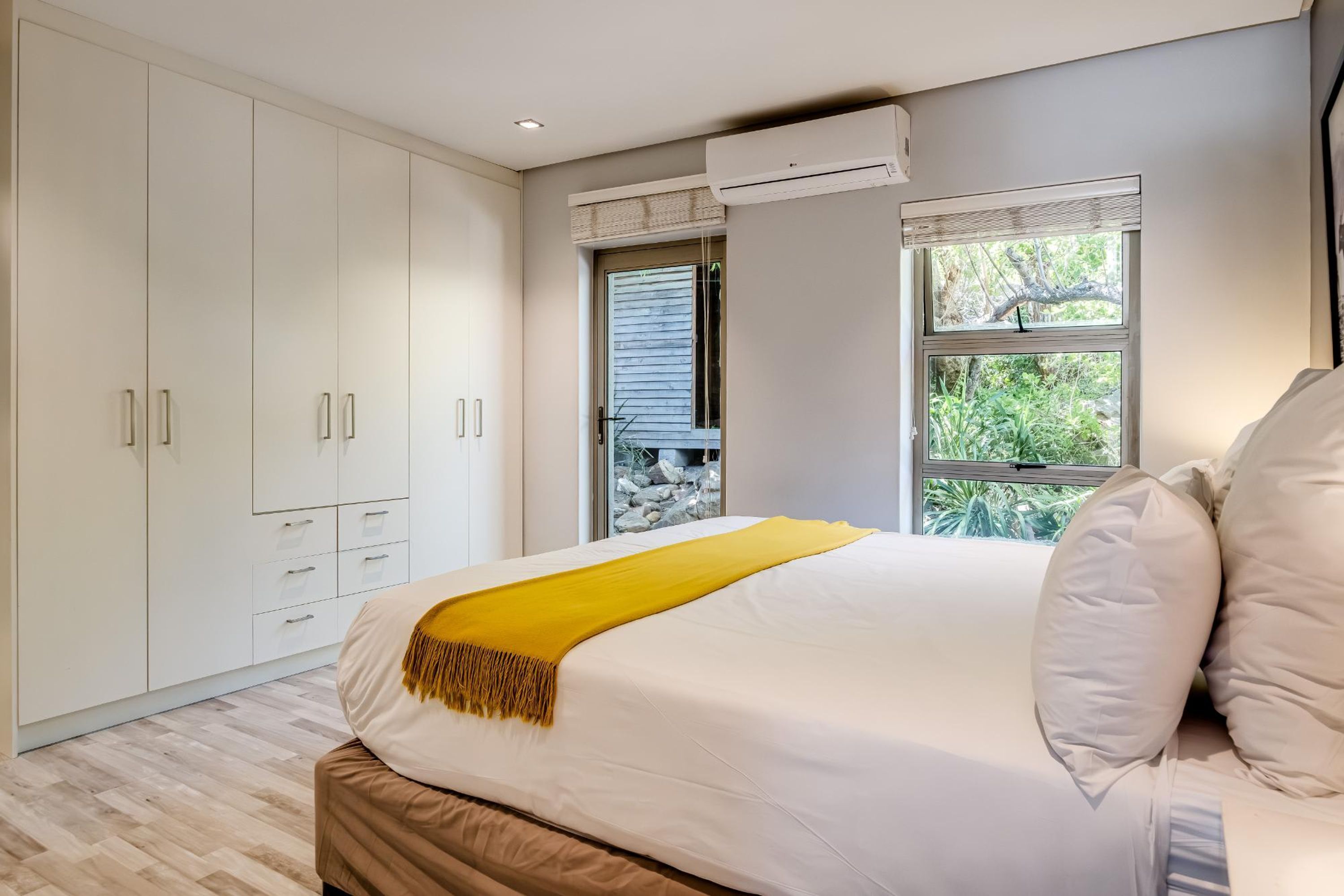 Ein Schlafzimmer mit Bett, weißem Wäscheschrank und Fenster mit Blick auf Grünflächen.