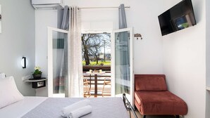 Une chambre d’hôtel avec un lit, un téléviseur fixé au mur et une vue sur une terrasse extérieure avec une table et des chaises.