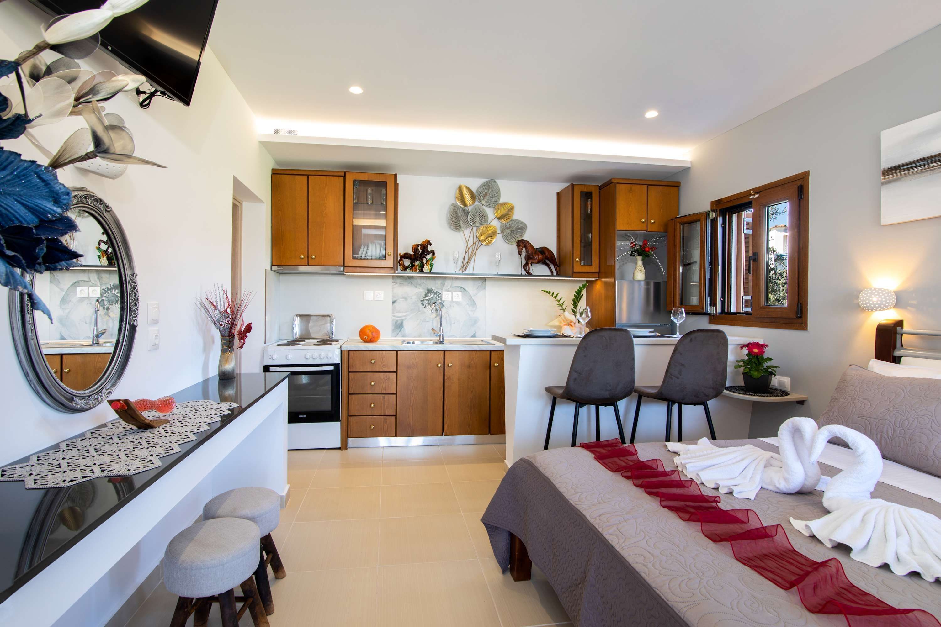 Habitación de hotel moderna con cocina, una mesa de comedor y una cama con toallas decorativas.