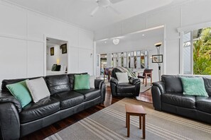 A spacious living room with a black leather sofa, a wooden coffee table, and a large window offering a view of the outdoors.