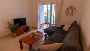 Una sala de estar con un sofá, un televisor sobre un mueble de madera, una mesa de centro y una planta en maceta.