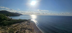 Paisaje costero con cielo despejado, mar tranquilo y terreno rocoso.