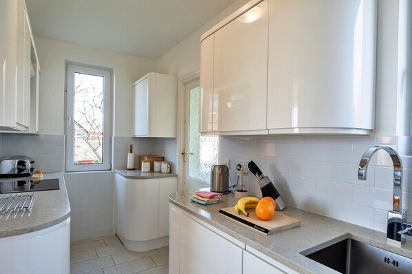 A modern kitchen with white cabinets, a built-in oven, a toaster, and a sink.