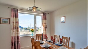 Comedor con una mesa de madera dispuesta para cuatro, dos sillas a cada lado, una lámpara colgante y vista a la playa a través de la ventana.