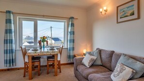 A cozy living room with a dining table, a sofa, and a view of the sea through large windows.