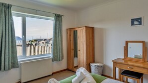 A room with a large window, wooden wardrobe, a small desk with a mirror, and a radiator.