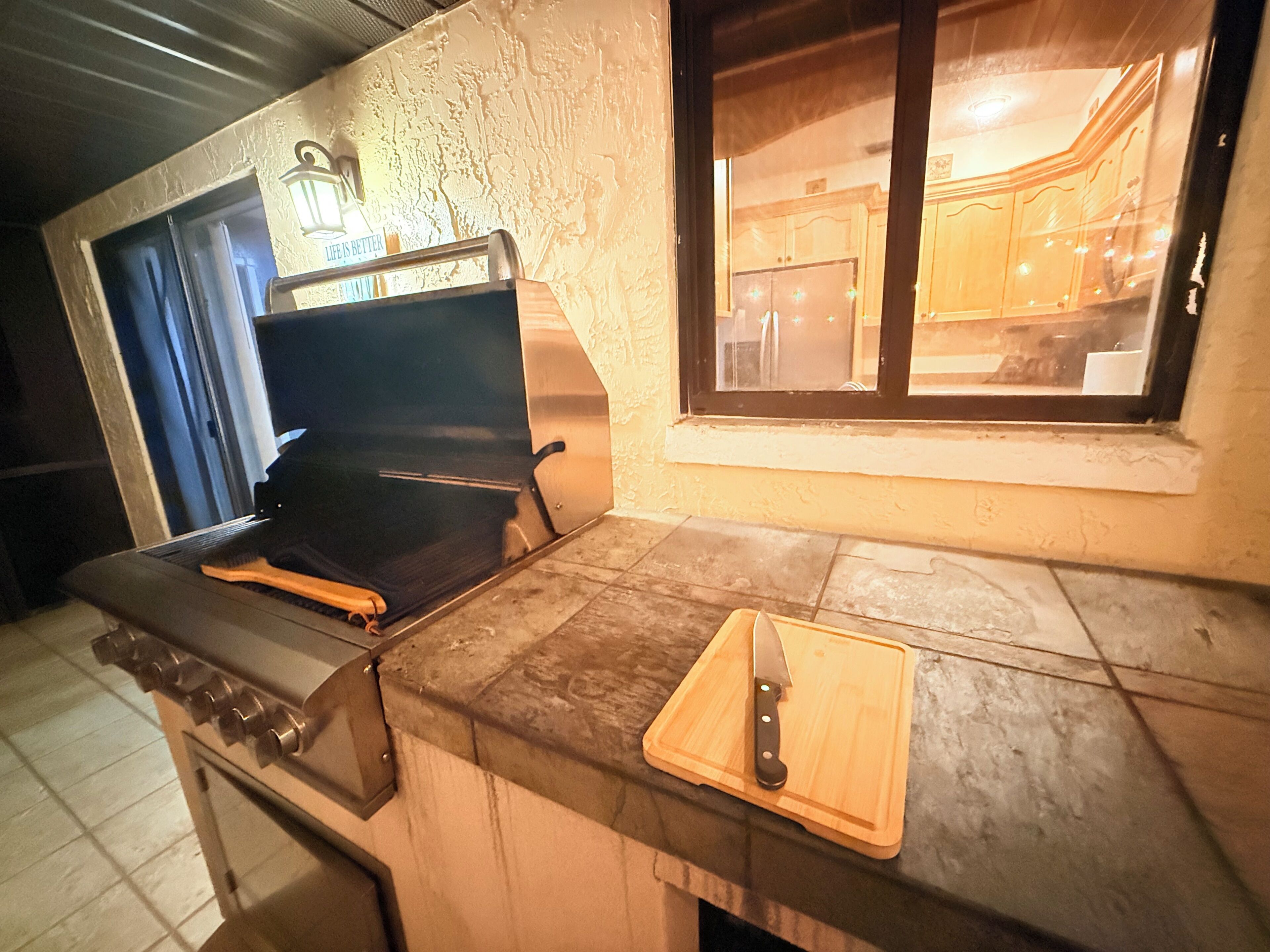 Eine Küche mit Grill, einem Fenster und einem Holztisch mit einem Messer.