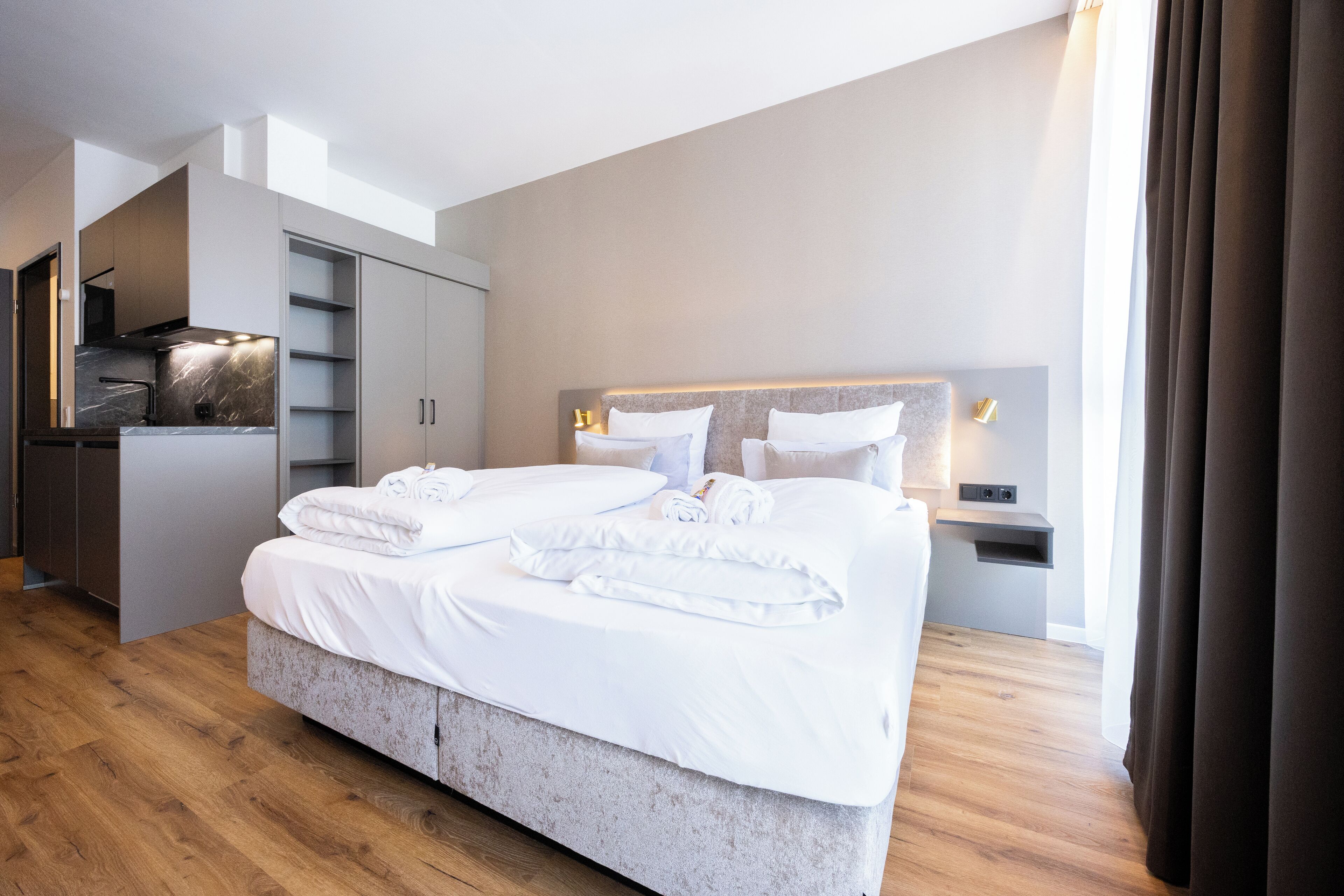 Een moderne hotelkamer met een groot bed, een inbouwkast en een kleine kitchenette.