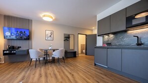 Moderni keittiö, jossa on tummat kaapit, marmoripintainen välitila ja sisäänrakennettu uuni. Keittiössä on myös ruokailutila, jossa on pöytä ja tuolit, sekä seinälle asennettu taulutelevisio.