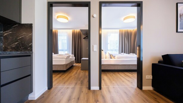 Moderni hotellihuone, jossa on puulattia, valkoisilla lakanoiden peitetty sänky, yöpöytä ja seinään kiinnitetty valaisin.