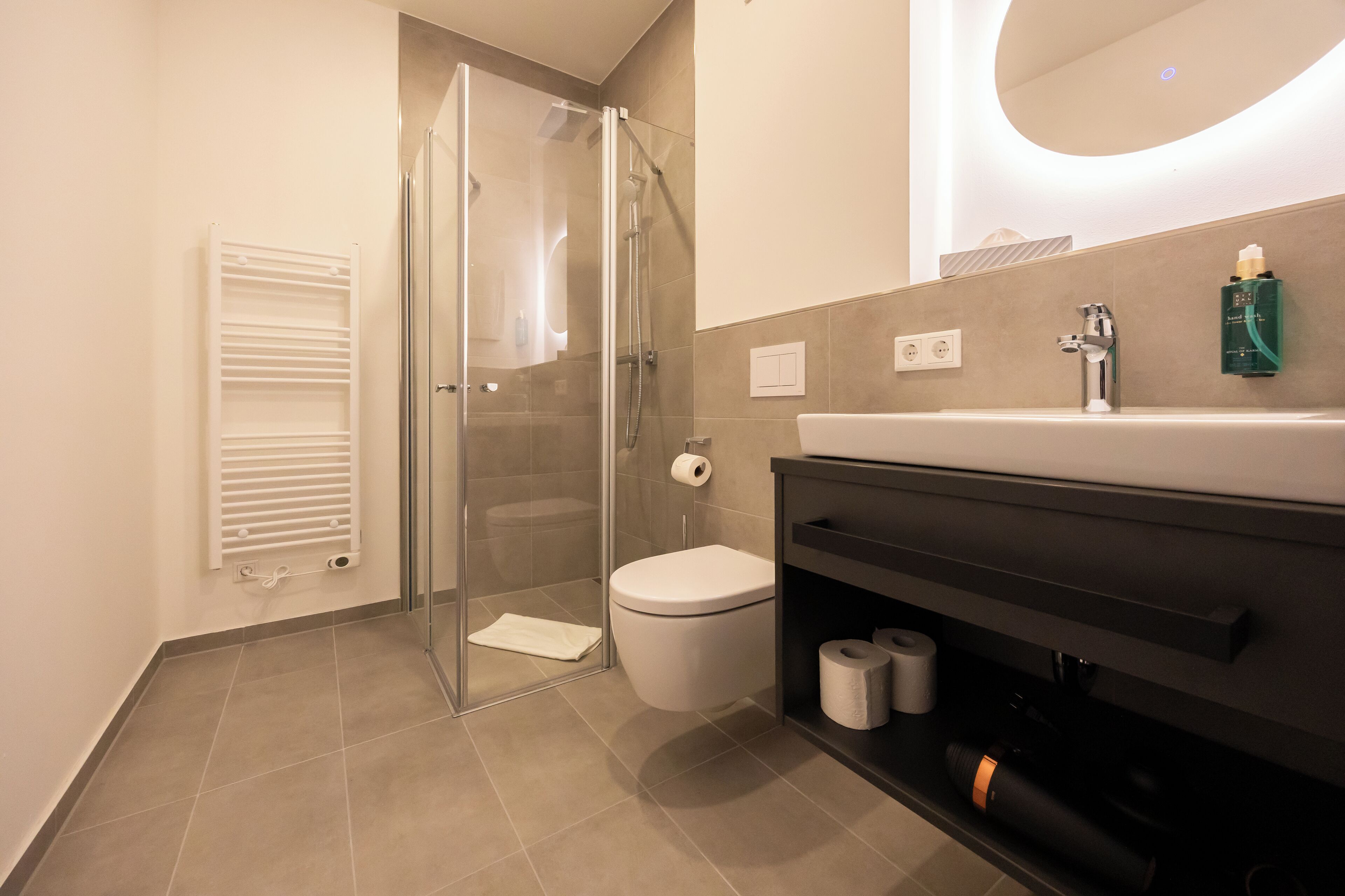 Une salle de bain moderne avec une douche à parois de verre, des toilettes, un lavabo avec un miroir au-dessus et un porte-serviettes.