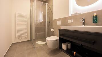 Une salle de bain moderne avec une douche à parois de verre, des toilettes, un lavabo avec un miroir au-dessus et un porte-serviettes.