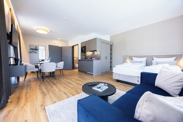 A modern hotel room with a dining area, kitchenette, and a large bed.