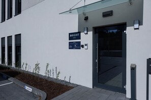 A modern building entrance with a glass canopy, a sign indicating 'BRIGHT' with parking information, and a security keypad.