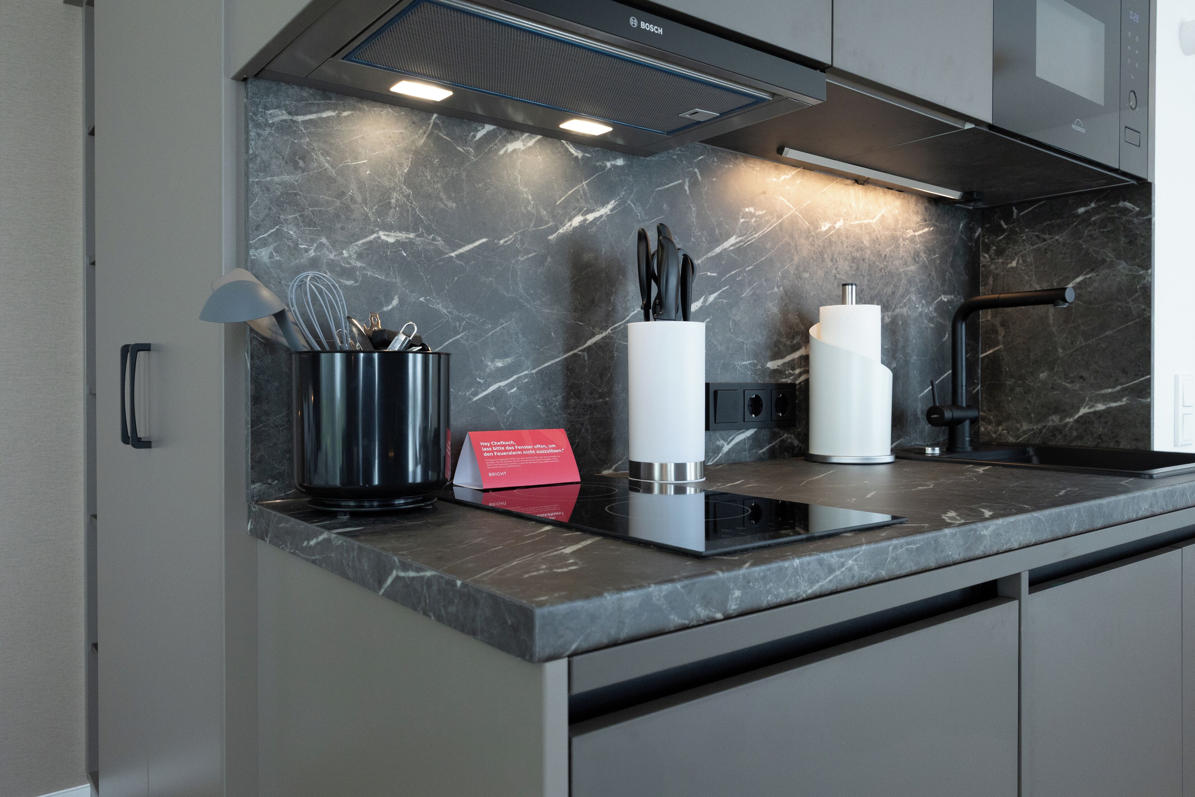 A modern kitchen with a marble backsplash, stainless steel appliances, and a black induction cooktop.