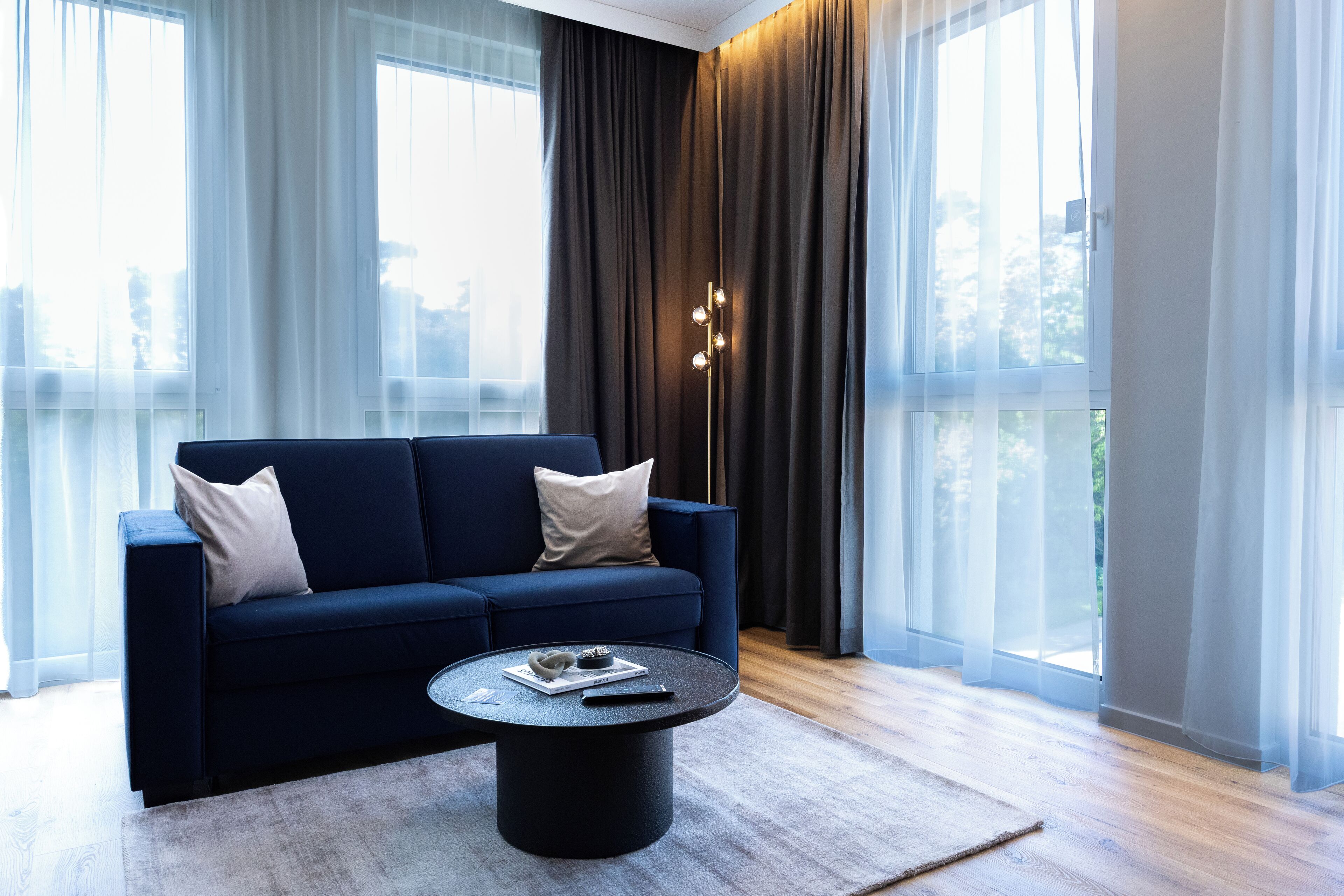 A modern living room with a dark blue sofa, a round coffee table, and sheer curtains.