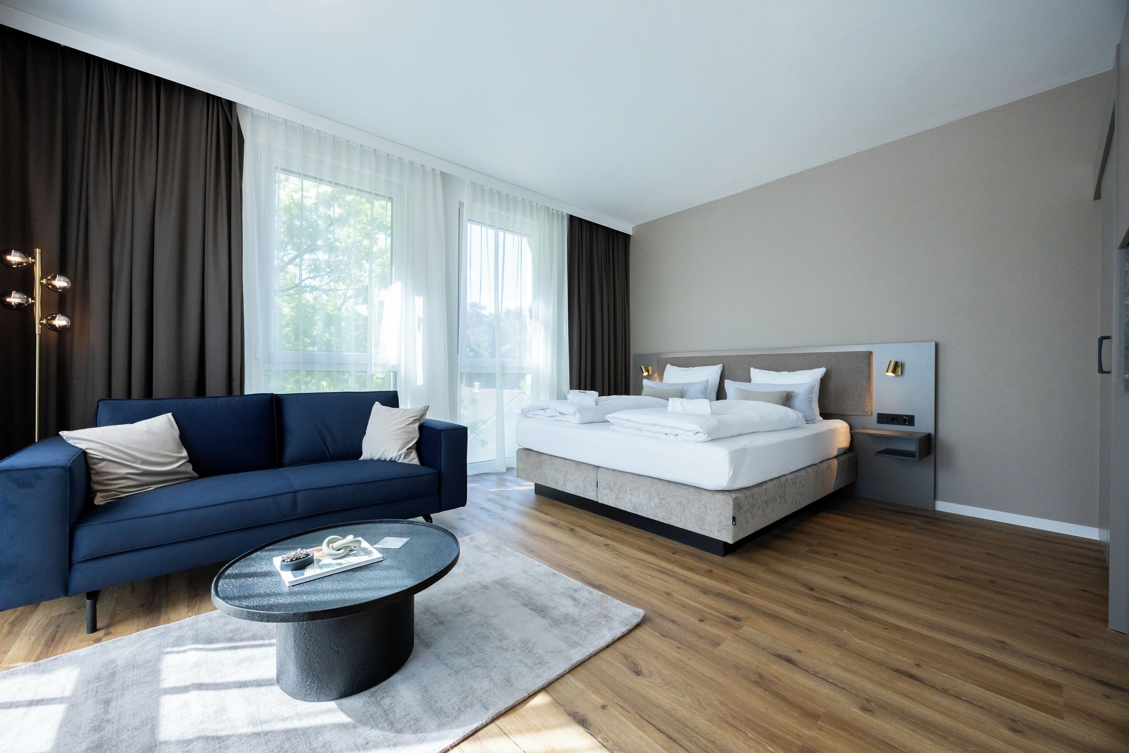 Une chambre à coucher moderne avec un grand lit, un canapé bleu et une table basse ronde.