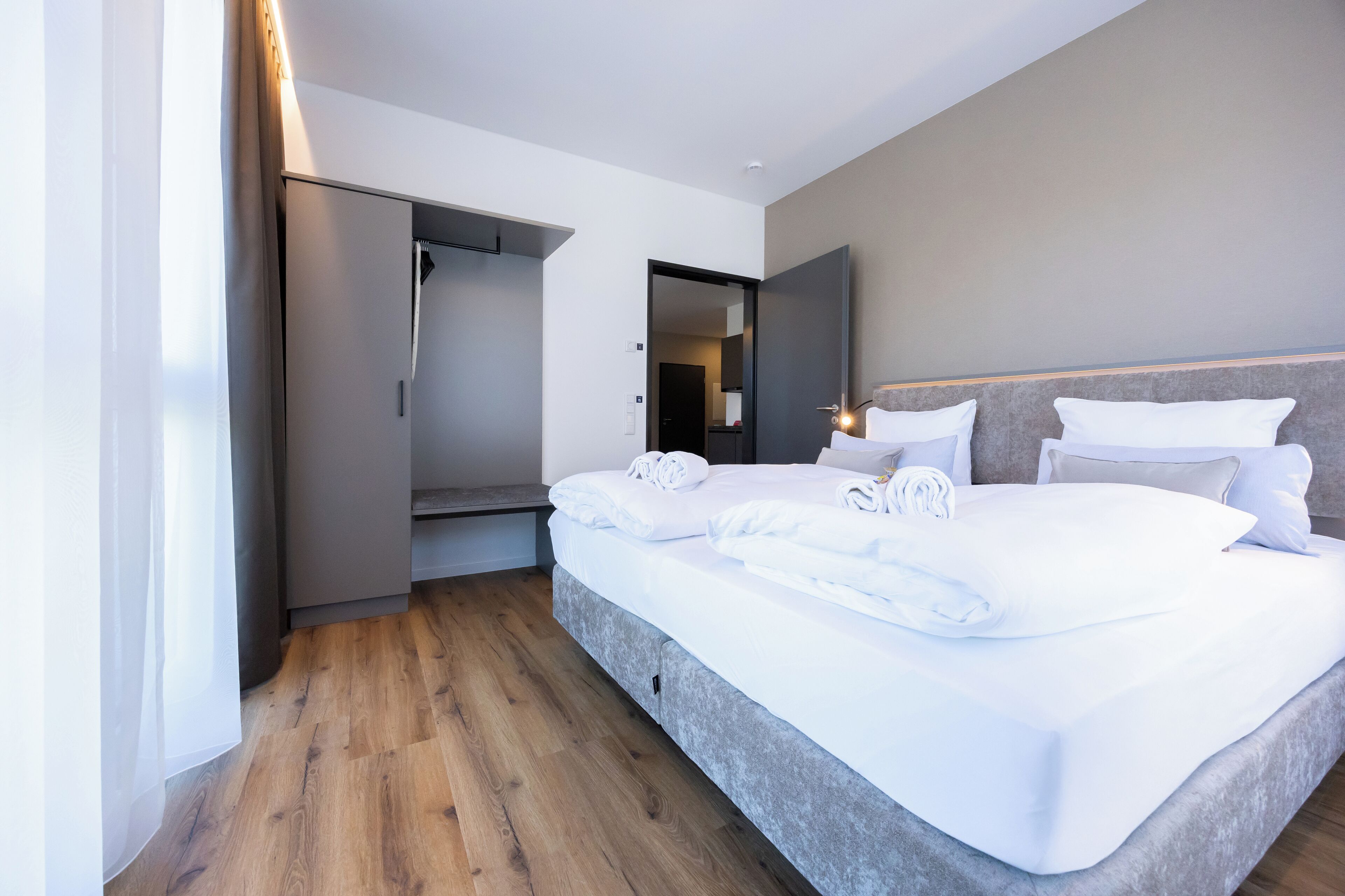 A modern hotel room with a large bed, a wardrobe, and a mirror.
