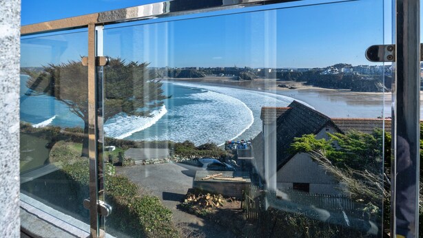 A coastal view from a high-rise building with a clear sky, a beach, and a small house with a sloped roof.