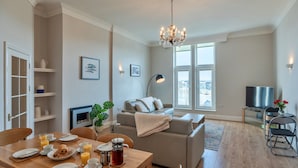 A modern living room with a dining area, a sofa, a TV, and a chandelier.