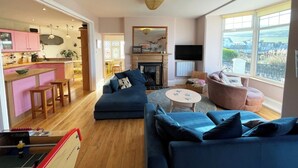 Een moderne woonkamer met een blauwe bank, een roze fauteuil en een eethoek met roze kasten.
