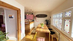 Een smalle keuken met roze kastjes, een houten eettafel met stoelen en een uitzicht op het buitenlands gebied door een raam met glas-in-lood.