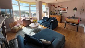 Een woonkamer met een bank, een bijzettafeltje, een tafelvoetbaltafel en uitzicht op het strand door grote ramen.